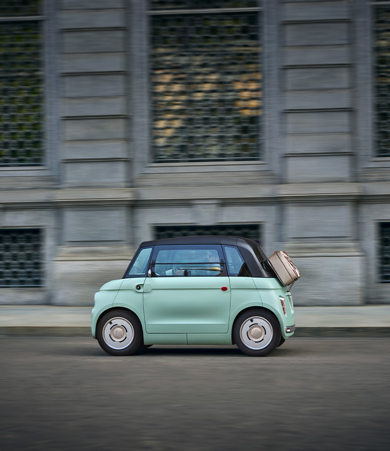 Fiat sett fra siden kjørende på vei med en koffert bak